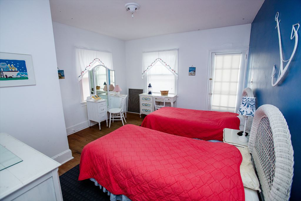 Nautical bedroom with two twin beds in red coverlets, a navy accent wall with rope-and-anchor decor and a white wicker headboard