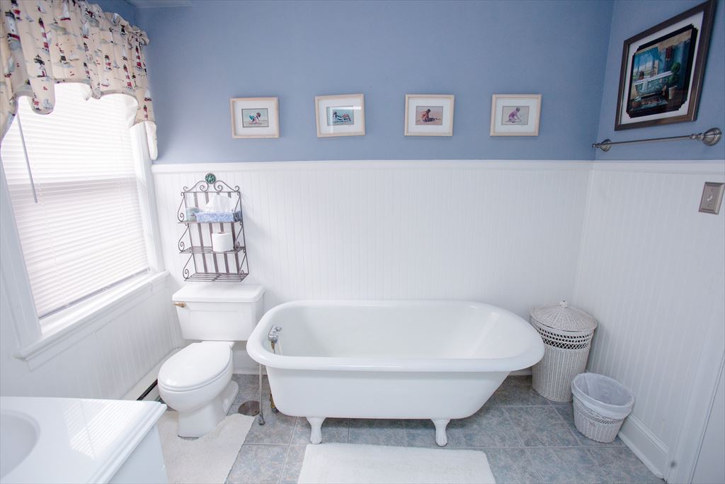Blue-and-white bathroom with a white clawfoot tub, beadboard wainscoting, framed beach prints and a patterned tile floor