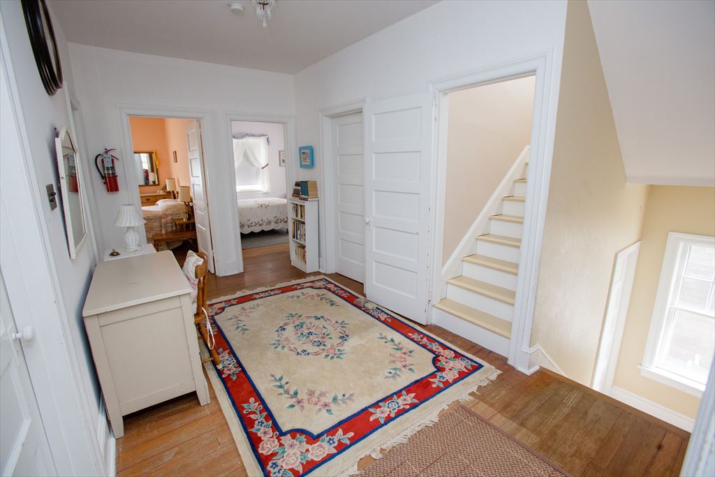 Upstairs hallway landing with hardwood floors, a floral area rug, a white dresser, a bookcase and a staircase