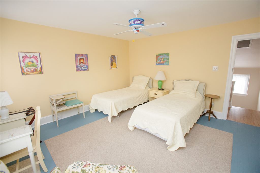 Yellow-walled children's bedroom with two twin beds in cream coverlets, a green lamp, a blue painted floor and a child's desk