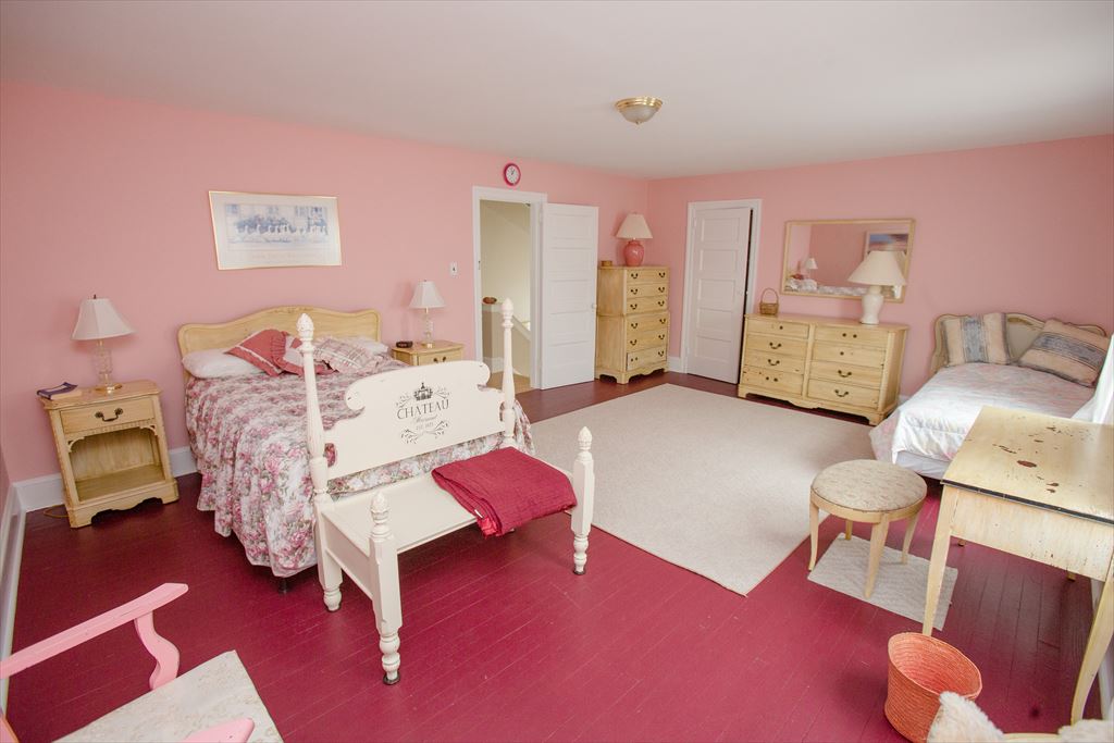 Spacious pink bedroom with a floral poster bed, light wood dressers and nightstands, a red painted floor and a white area rug