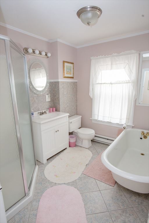 Pink-walled bathroom with a glass-door shower stall, a white vanity, an oval mirror and a clawfoot tub on a tile floor