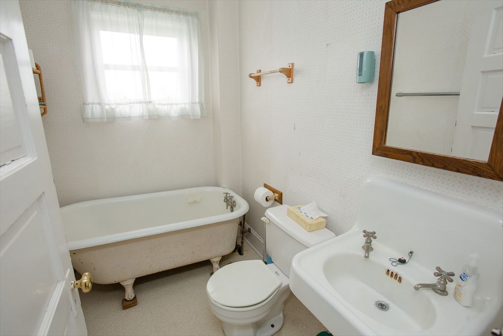 Vintage white bathroom with a claw-foot tub on brass feet, a pedestal sink with cross handles and a wood-framed mirror