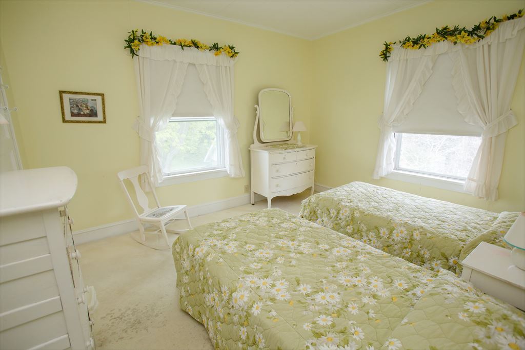Cheerful yellow bedroom with two twin beds in green daisy-print spreads, white painted dressers and a white rocking chair