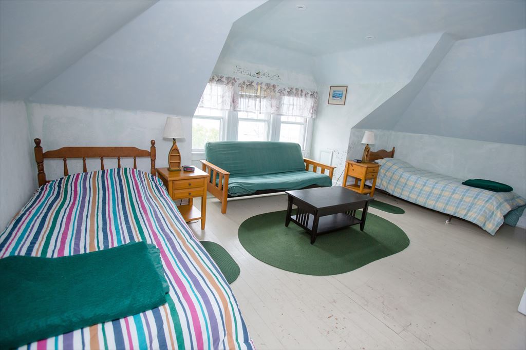 Large attic bedroom with sloped pale blue ceilings, a bed, a green futon and an extra twin bed, made for kids and big groups
