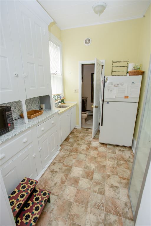 Galley pantry and kitchen area with white cabinetry, a refrigerator and an adjoining toilet room
