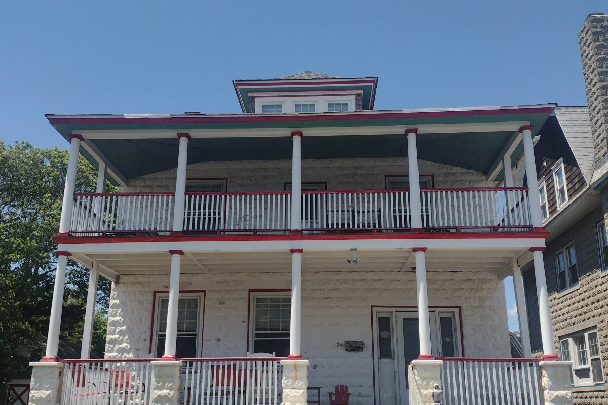 Front exterior of Sea Foam Manor, a three-story Cape May Victorian with double-stacked porches, bright red railings, sea-foam green steps and a dormered top floor
